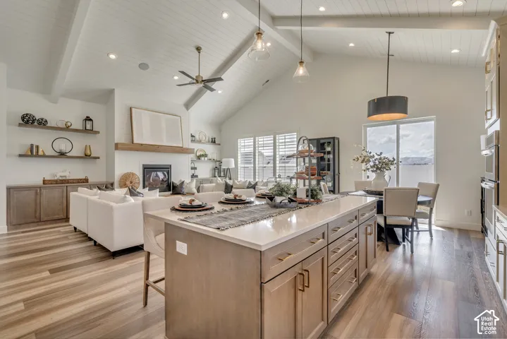 Spacious open-concept living area featuring a kitchen island with stone countertop, wood-finish flooring, vaulted shiplap ceiling, and built-in fireplace