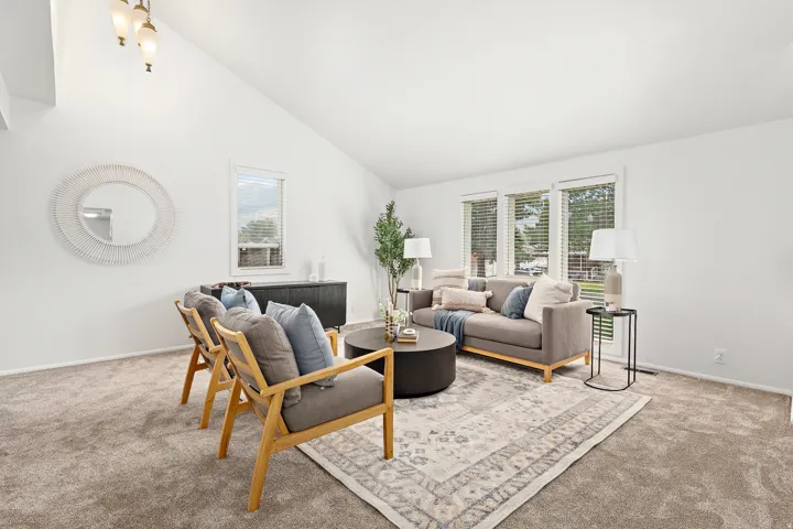 Spacious living area featuring vaulted ceilings, plush carpet flooring, and abundant natural light from multiple windows
