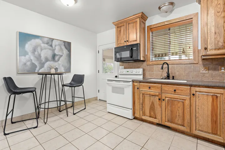Kitchen featuring light wood cabinetry, a built-in black microwave, a single basin sink with a gooseneck faucet, a tile backsplash, and light-toned floor tiles