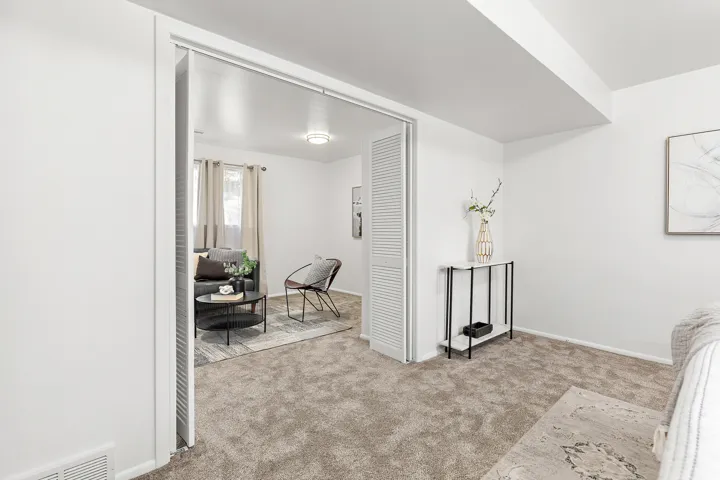 Carpeted room featuring a white ceiling and walls, with an open doorway revealing a second room with a window and a ceiling light fixture