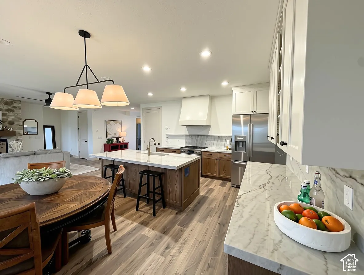 Spacious open-concept kitchen featuring an oversized island with seating, white cabinetry, integrated stainless steel appliances, and wood-finish flooring