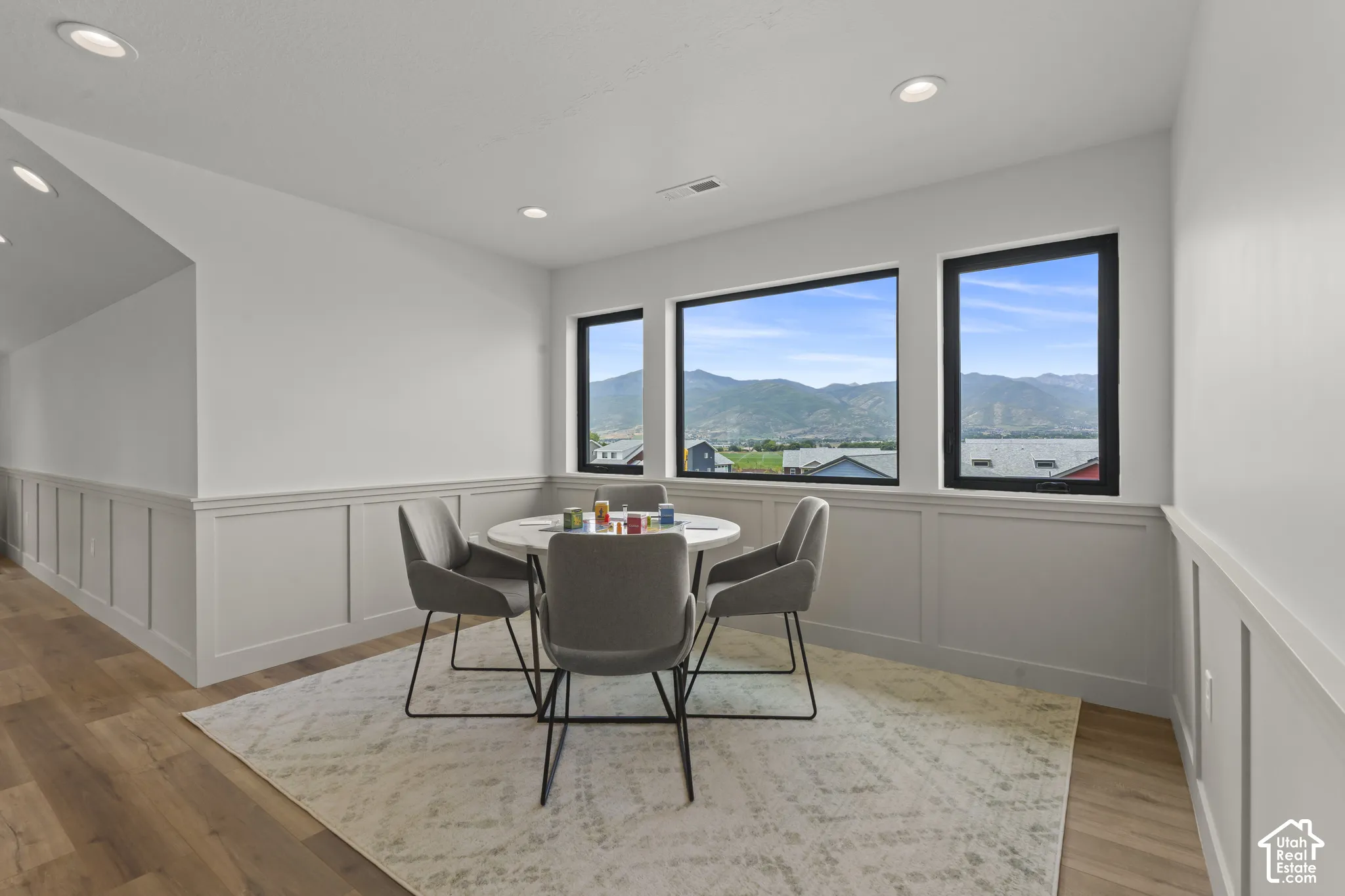 Room featuring three large windows showcasing a mountain backdrop, wainscoting, recessed lighting, and wood-finish flooring