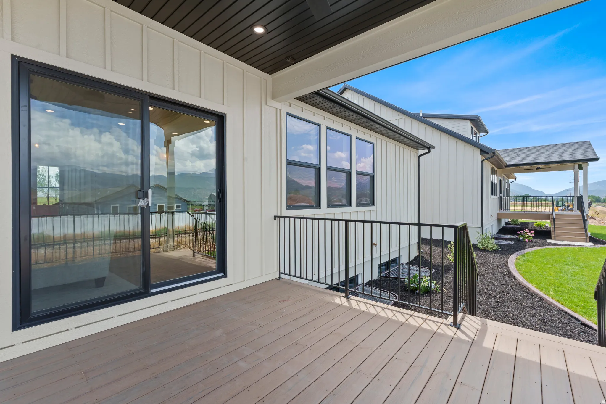 Spacious outdoor deck featuring wood-finish decking, black metal railings, and a sliding glass door