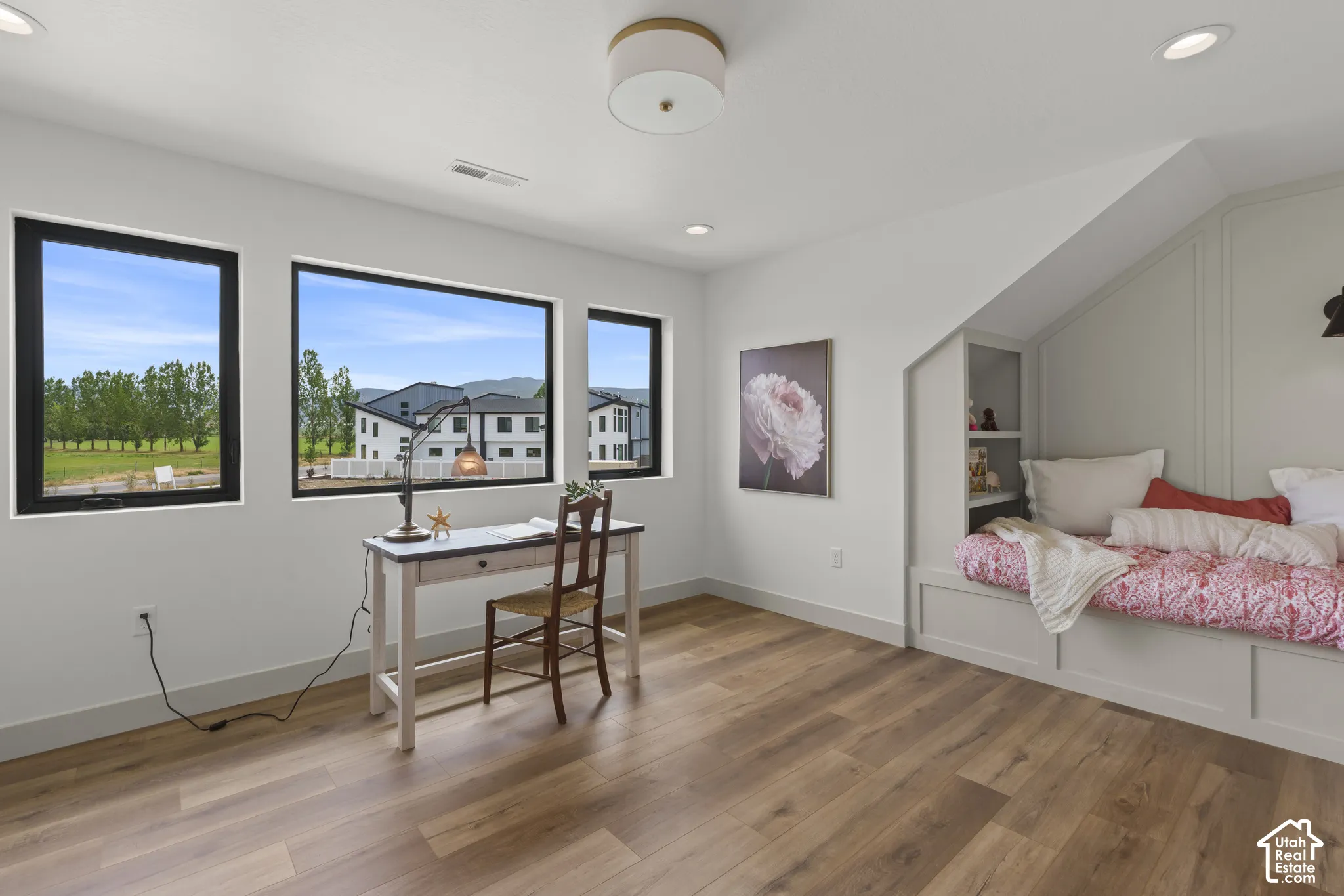 Room featuring wood-finish flooring, a built-in daybed with integrated shelving, and three large windows with black trim