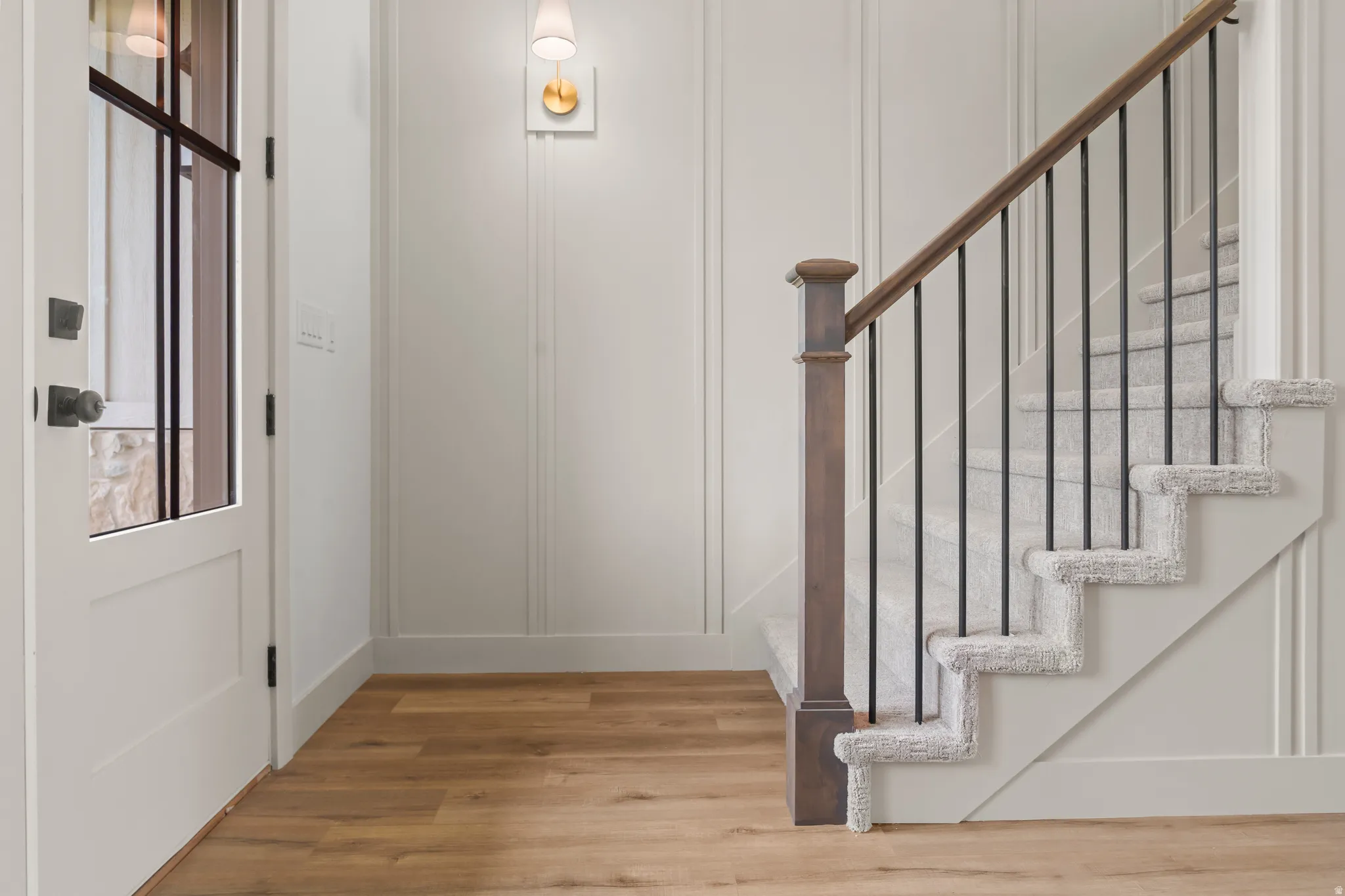 Staircase featuring wood newel post and handrail with black iron balusters, complemented by light grey carpeted treads