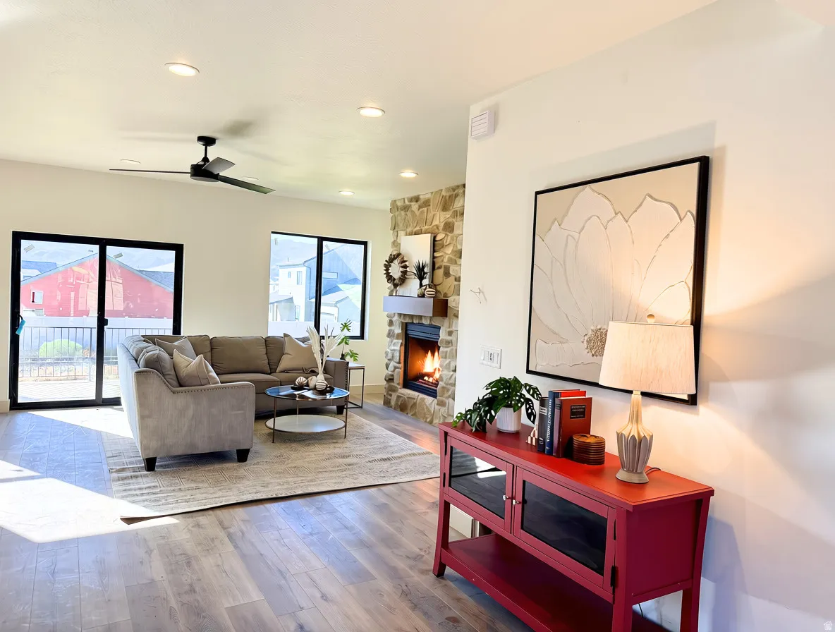 Living area featuring wood-finish flooring, a stone-surround fireplace with a wood mantle, and a ceiling fan with integrated lighting