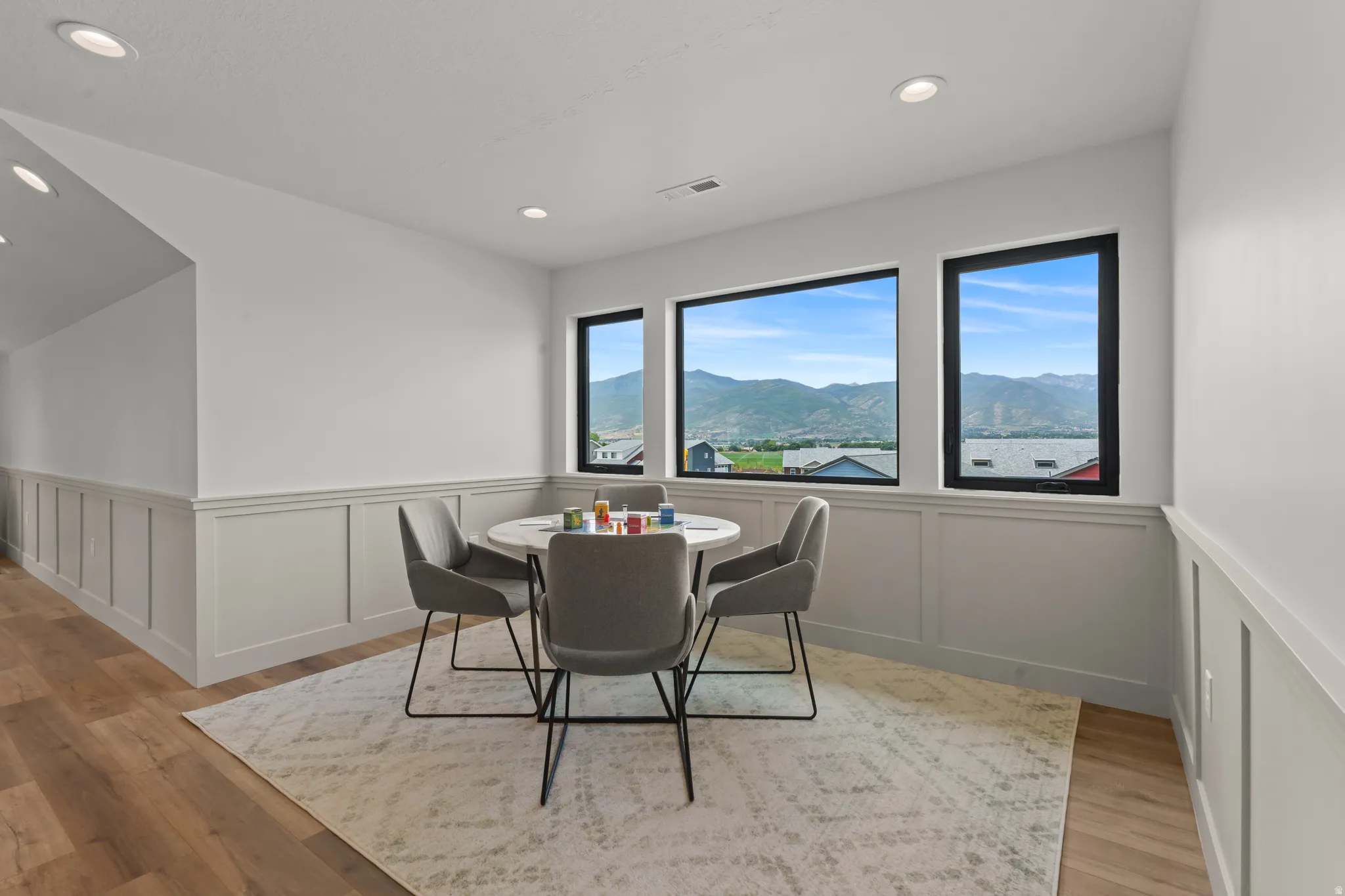 Room featuring three large windows showcasing a mountain backdrop, wainscoting, recessed lighting, and wood-finish flooring