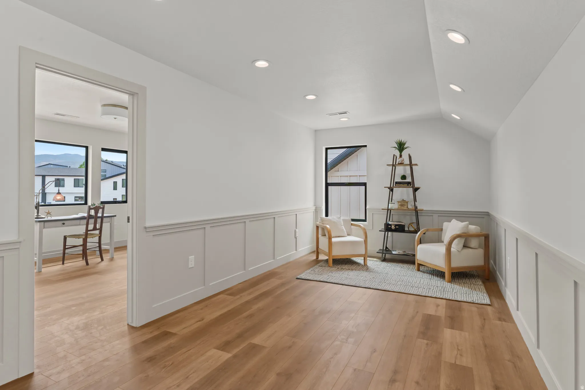Spacious interior featuring wood-finish flooring, white walls with wainscoting, recessed lighting, and a vaulted ceiling