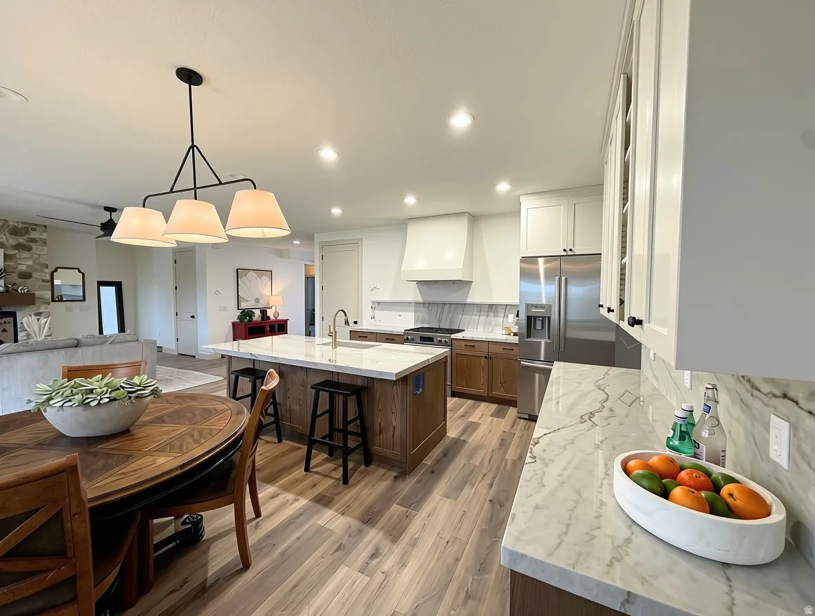 Spacious open-concept kitchen featuring an oversized island with seating, white cabinetry, integrated stainless steel appliances, and wood-finish flooring