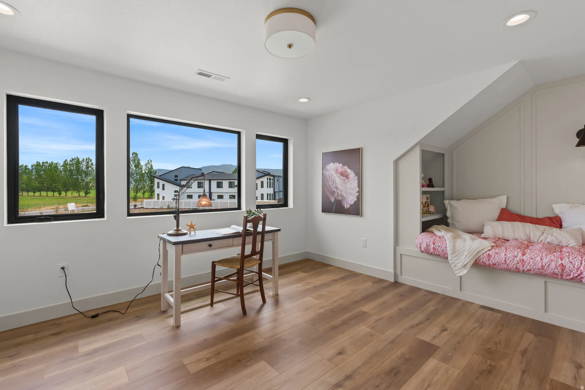 Room featuring wood-finish flooring, a built-in daybed with integrated shelving, and three large windows with black trim