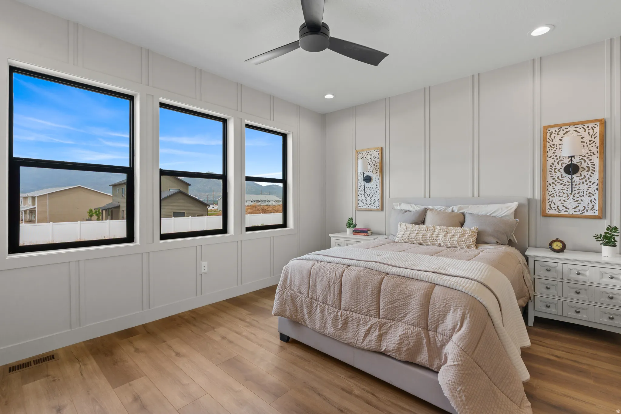 Spacious room featuring three large windows with black frames, wood-finish flooring, a modern ceiling fan, recessed lighting, and decorative wall paneling