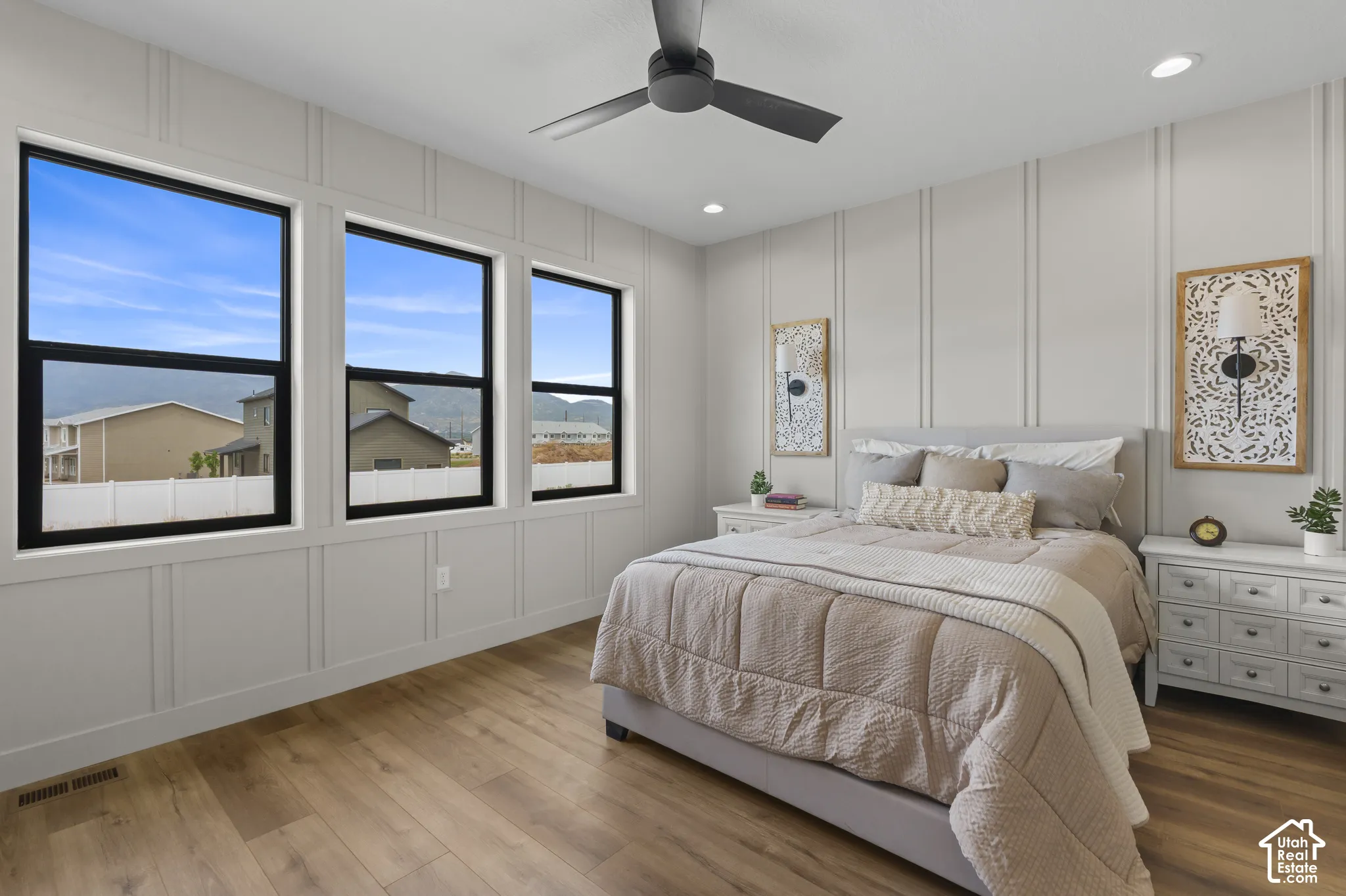 Spacious room featuring three large windows with black frames, wood-finish flooring, a modern ceiling fan, recessed lighting, and decorative wall paneling