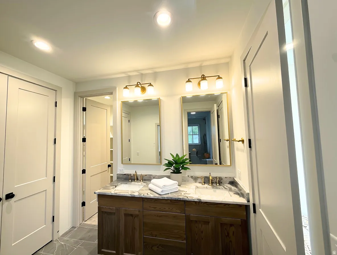 Dual vanity featuring wood cabinetry, marble-finish countertop, and brass fixtures