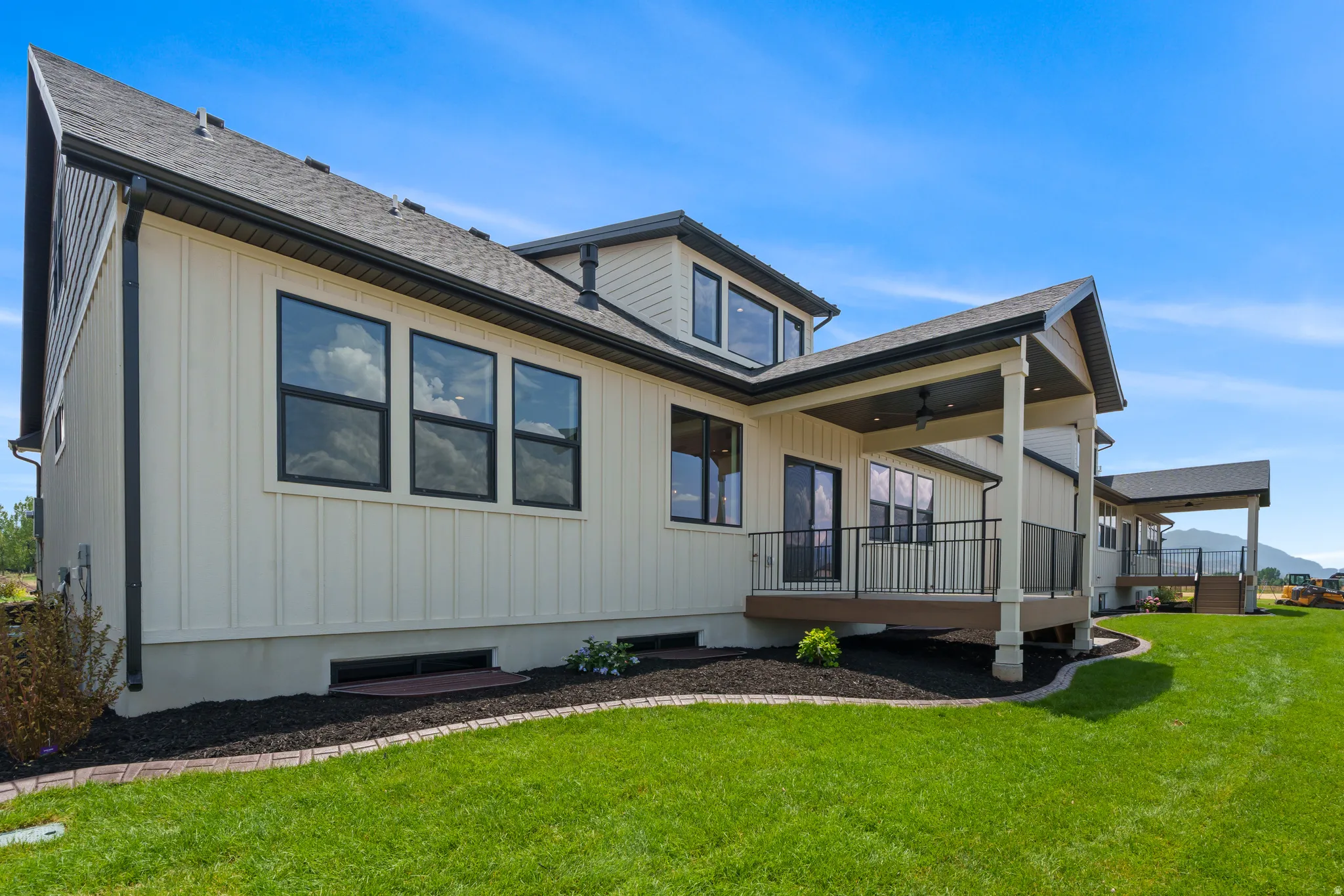 Exterior showcasing light-colored vertical siding, dark-framed windows, and a covered patio with dark railings