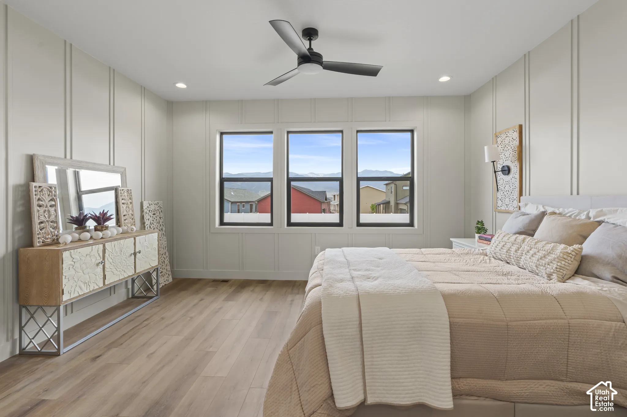 Bedroom featuring three windows with dark frames, wood-finish flooring, and vertical panel accent walls
