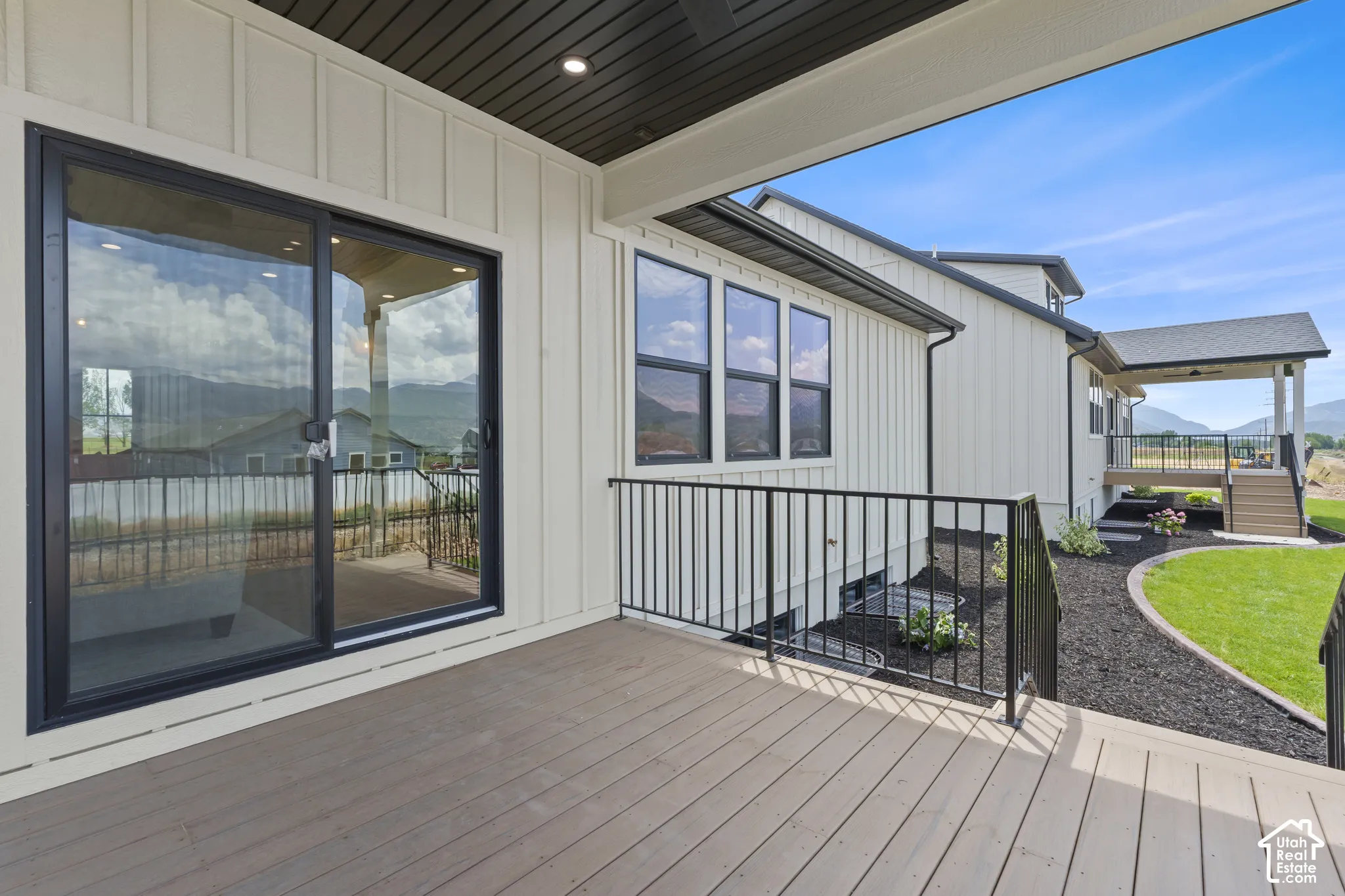 Spacious outdoor deck featuring wood-finish decking, black metal railings, and a sliding glass door