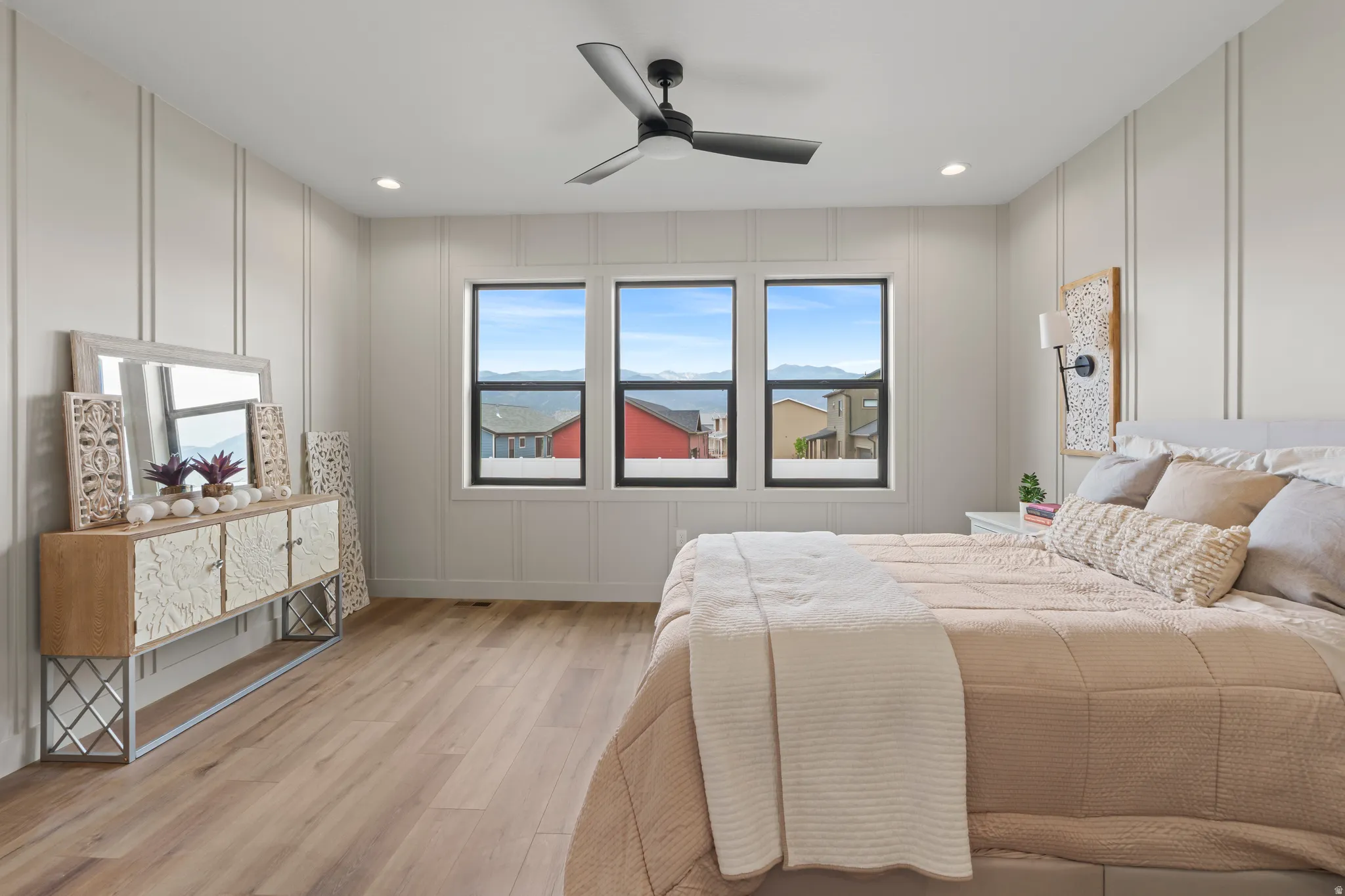 Bedroom featuring three windows with dark frames, wood-finish flooring, and vertical panel accent walls