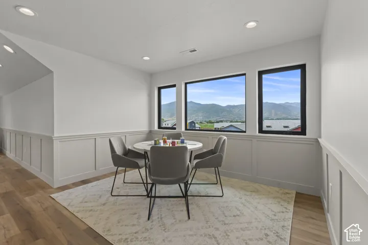 Room featuring three large windows showcasing a mountain backdrop, wainscoting, recessed lighting, and wood-finish flooring