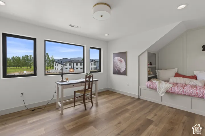 Room featuring wood-finish flooring, a built-in daybed with integrated shelving, and three large windows with black trim