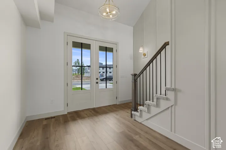 Entryway featuring double doors with divided lites, wood-finish flooring, a contemporary chandelier, a staircase with carpeting and wrought iron balusters, and wainscoting