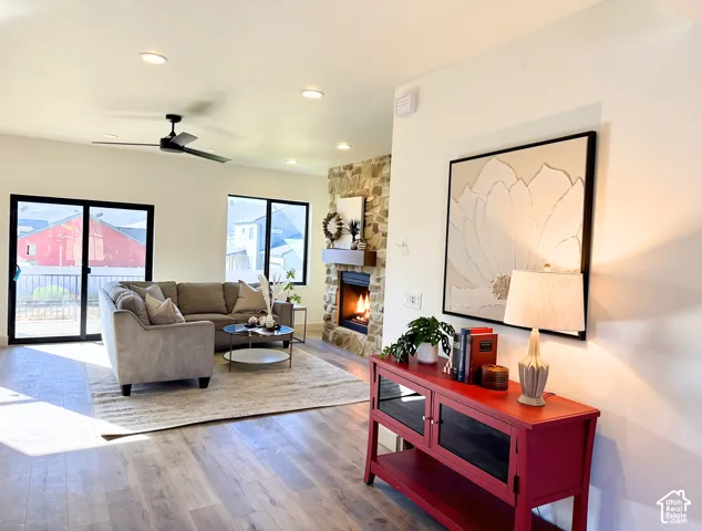 Living area featuring wood-finish flooring, a stone-surround fireplace with a wood mantle, and a ceiling fan with integrated lighting