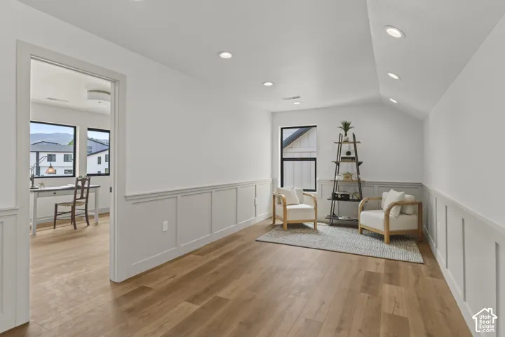Spacious interior featuring wood-finish flooring, white walls with wainscoting, recessed lighting, and a vaulted ceiling