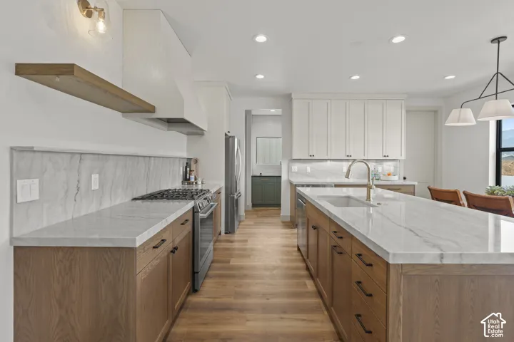 Gourmet kitchen with wood-finish flooring, a substantial center island with integrated sink, stone countertops, and a full-height stone backsplash