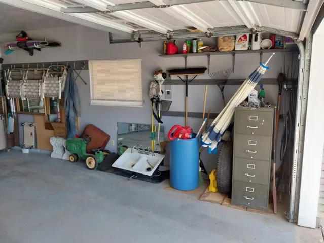 Garage space with a window featuring horizontal blinds, upper shelving, and a concrete floor
