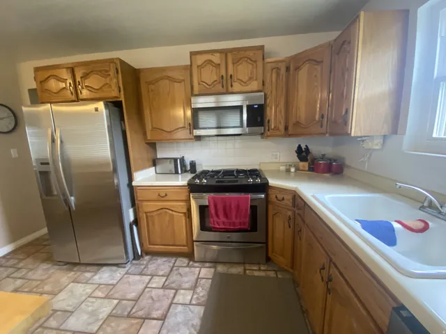 Kitchen featuring wood cabinetry, stainless steel appliances, tile floor and gas range.