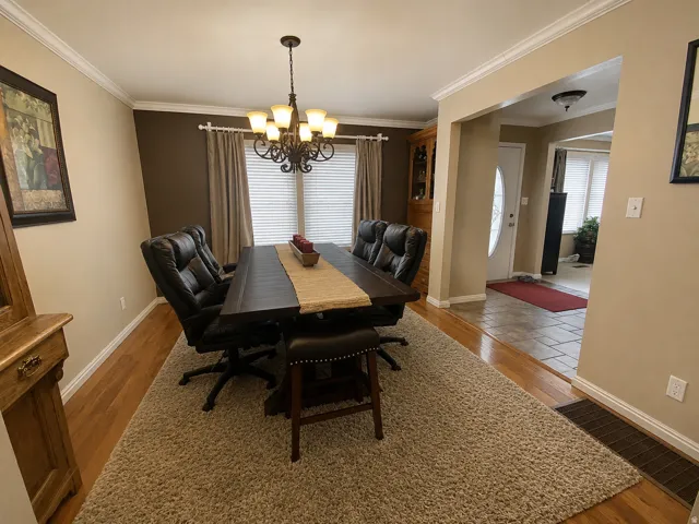 Dining area with wood-finish flooring, crown molding, and a chandelier