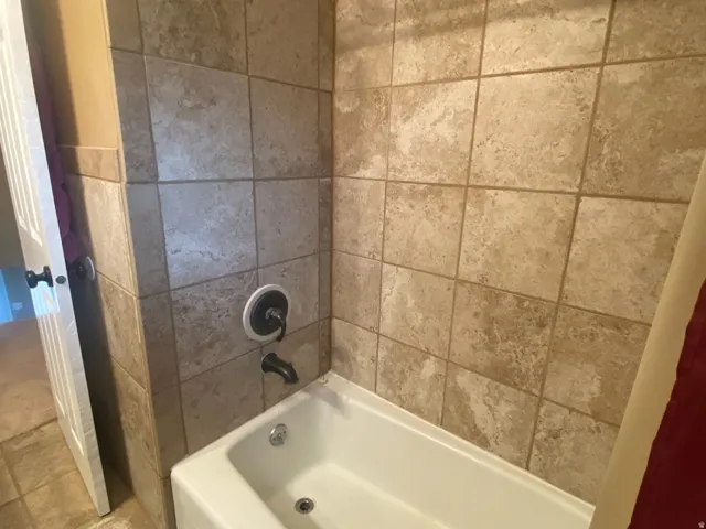 Bathtub with tile surround featuring a bronzed shower head and tub filler