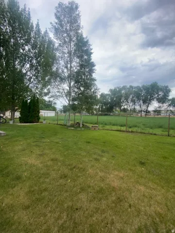 Expansive lawn with mature trees and a wire fence bordering a green field