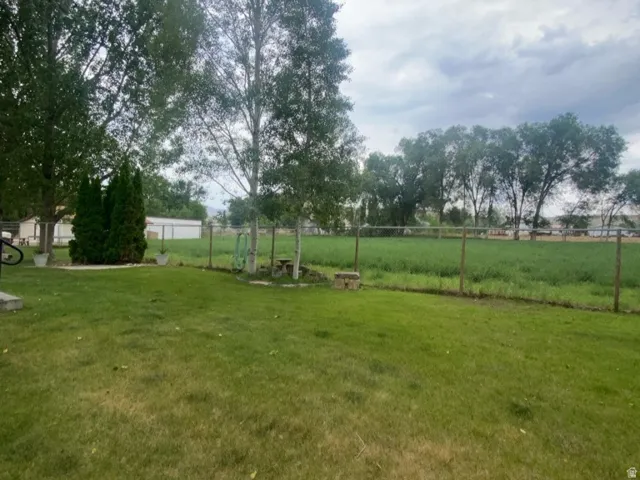 Expansive lawn with mature trees and a wire fence bordering a green field