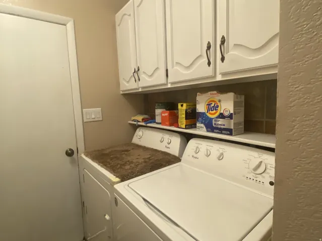 Laundry area featuring overhead white cabinetry with decorative panels, a built-in shelf, and tile flooring. Laundry room is off the kitchen area.