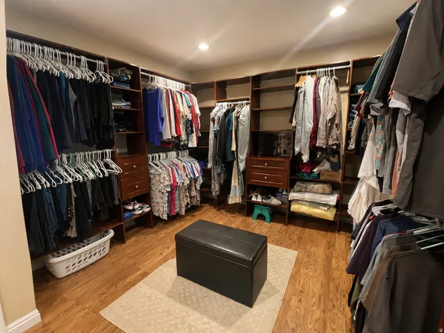 Spacious walk-in closet featuring extensive built-i shelving, multiple hanging rods, drawers, recessed lighting and wood finished flooring.