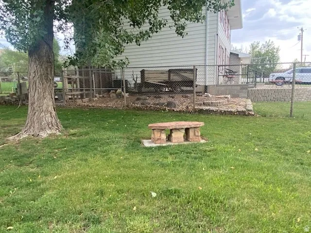 Spacious yard featuring a mature tree, stone bench, and chain-link fencing enclosing a paved patio area