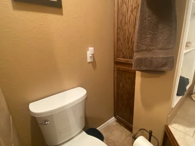Bathroom featuring a white toilet, warm-toned walls, wood-finish cabinetry, and tile flooring