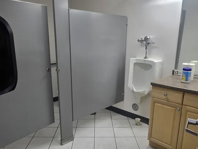 Commercial restroom featuring light-toned square floor tiling and light wood-finish cabinetry