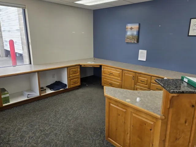 Functional office space featuring extensive built-in cabinetry with wood-finish doors and drawers, a corner desk area, and a reception counter with a stone-finish top