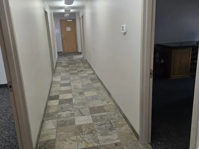 Corridor featuring square tile flooring, neutral wall tones, and overhead lighting fixtures