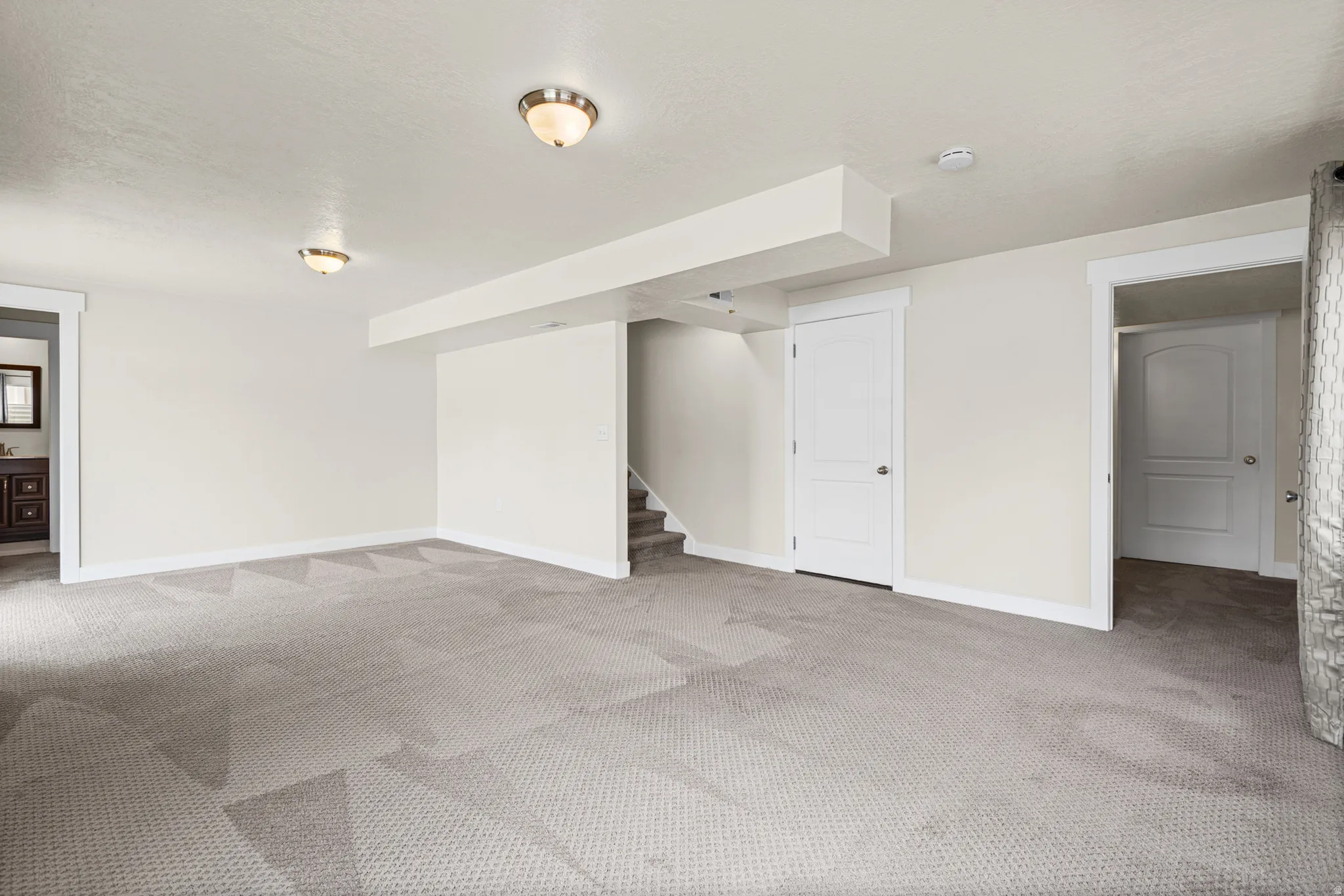 Spacious room featuring light-colored walls, patterned carpeting, and white trim