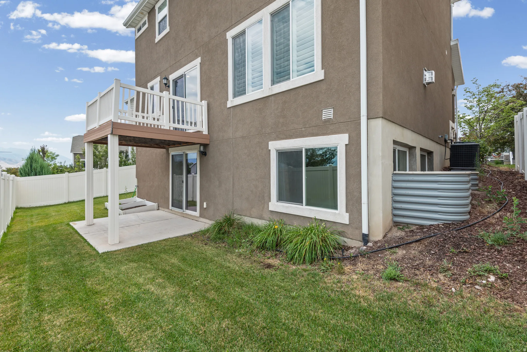 Rear exterior with a concrete patio, covered by a white-railed deck, and a sliding glass door entry