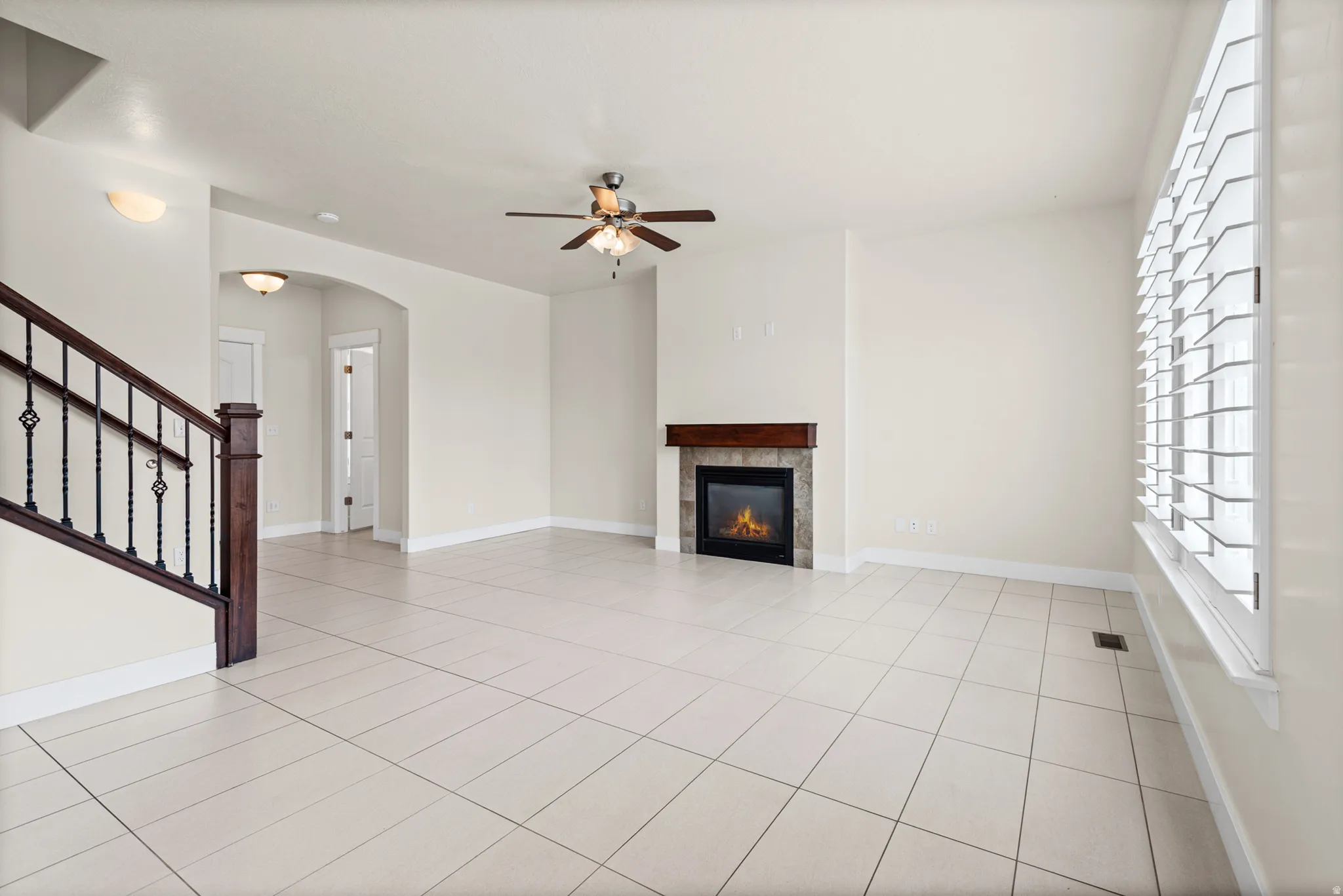 Spacious living area featuring light-toned tile flooring, a fireplace with a stone surround and wood mantel, and a ceiling fan