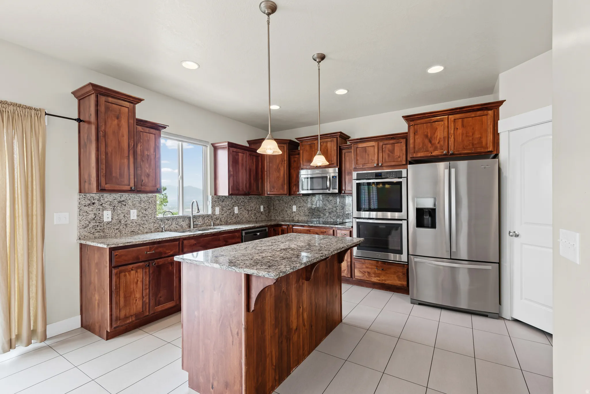 Kitchen featuring wood cabinetry, granite countertops, tile flooring, and stainless steel appliances including a built-in double oven and microwave