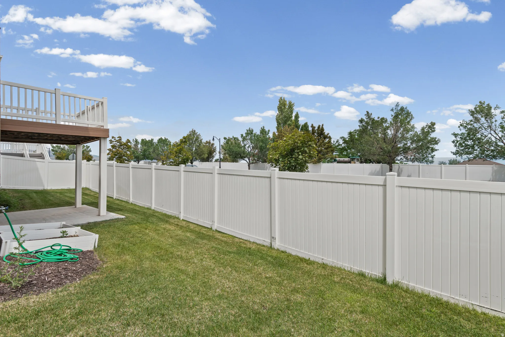 Expansive backyard featuring a manicured lawn, full privacy fencing, a concrete patio, and an elevated wood-finish deck with white railings