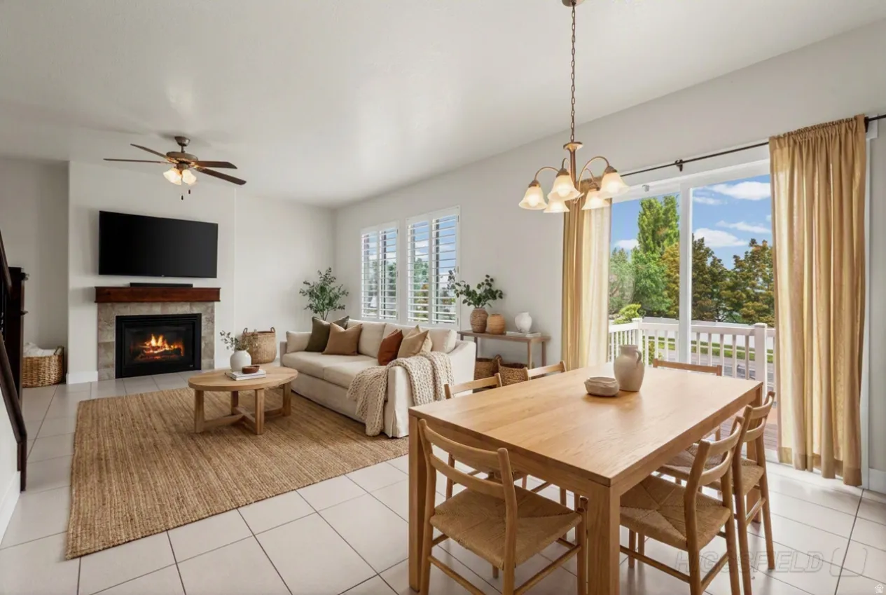 Living and dining area featuring a stone-surround fireplace with a wood mantel, ceiling fan, and sliding glass doors opening to a deck. Virtually staged.