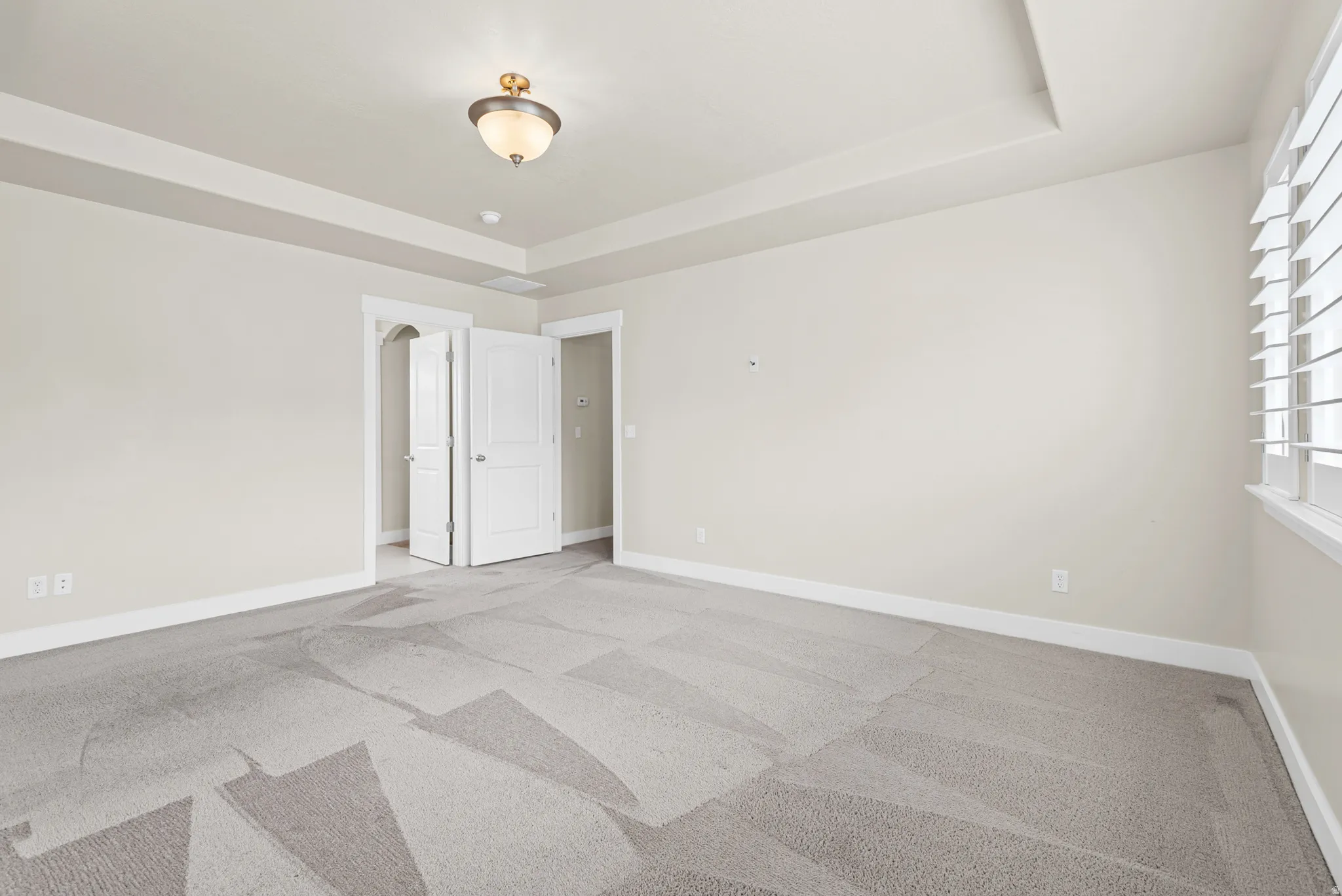 Spacious room featuring a tray ceiling, contemporary ceiling light fixture, white plantation shutters, and light-toned walls