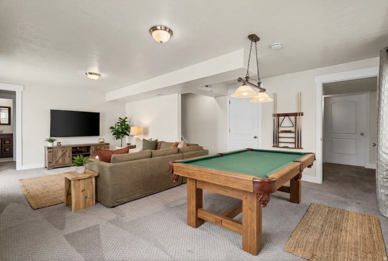 Expansive recreational area featuring a billiard table with a wood frame, a media console with a television, plush carpeting, and recessed lighting fixtures. Virtually staged.