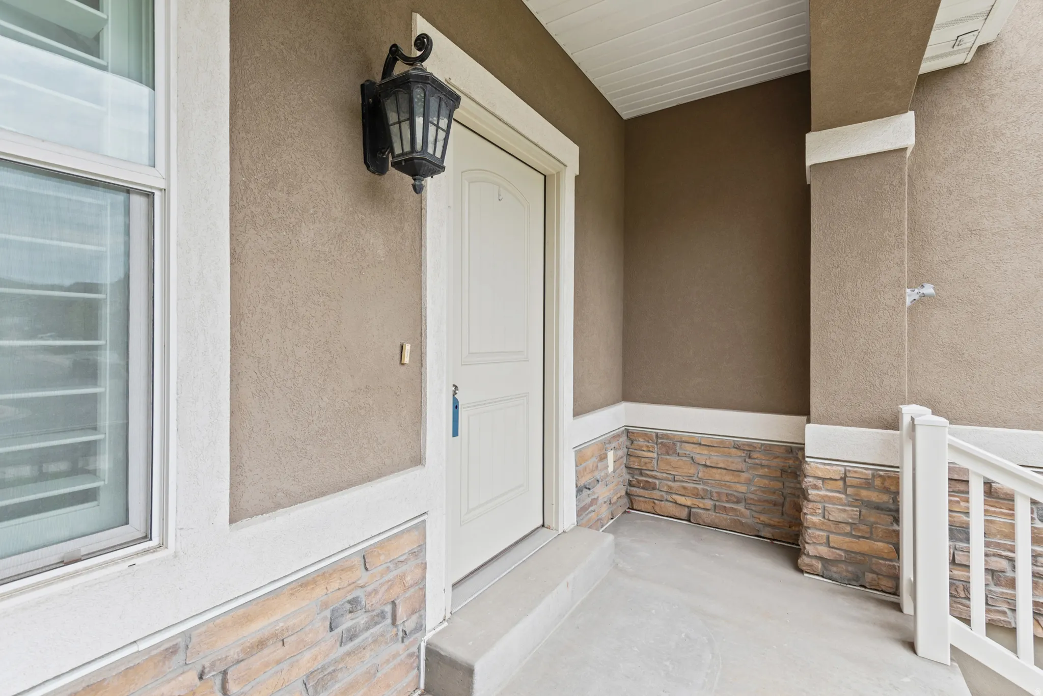 Inviting front porch featuring a white panel door, stucco siding, and a stone veneer base