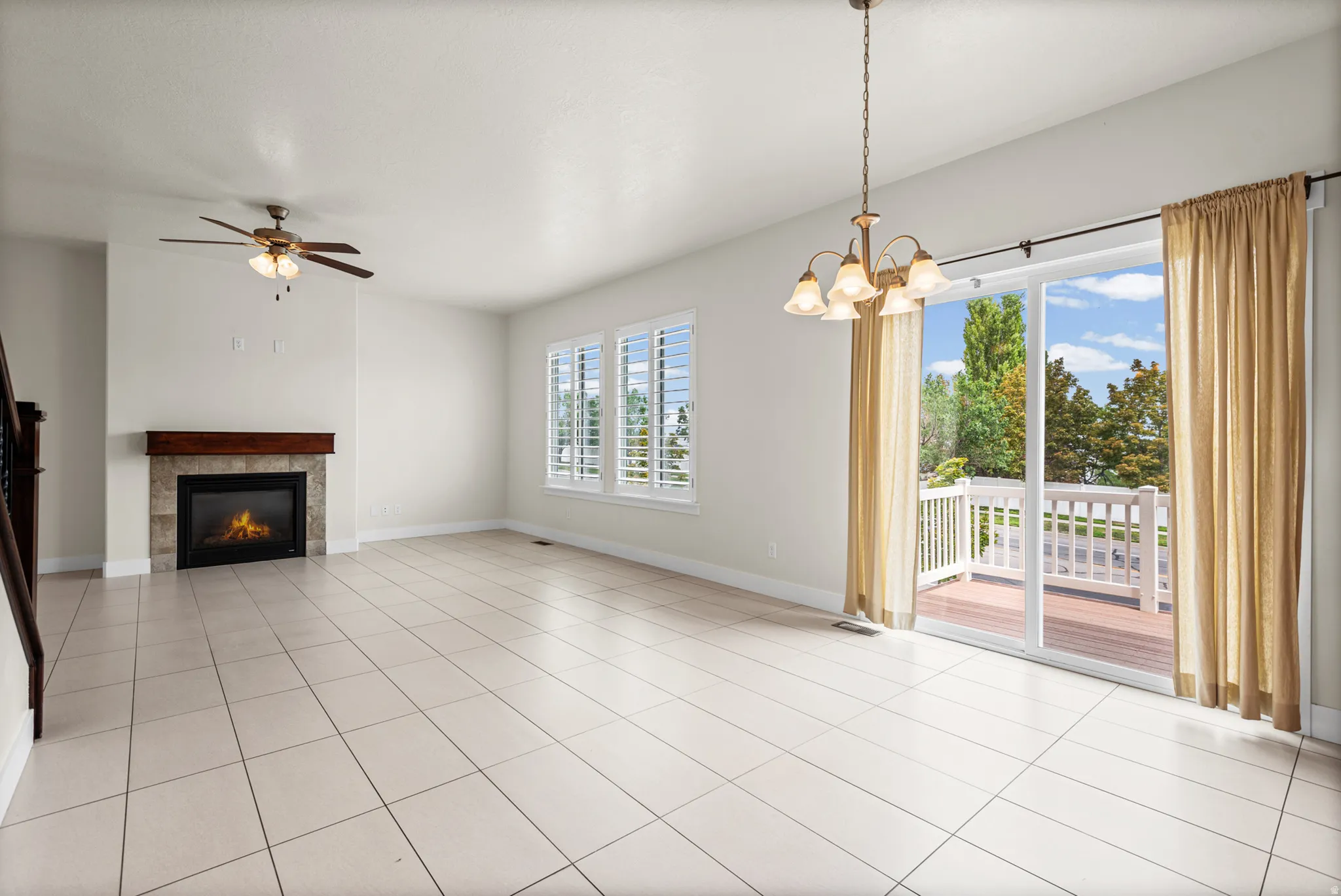 Spacious room featuring light-colored square tile flooring, a fireplace with a stone surround and wood mantel, and multiple windows with white plantation shutters